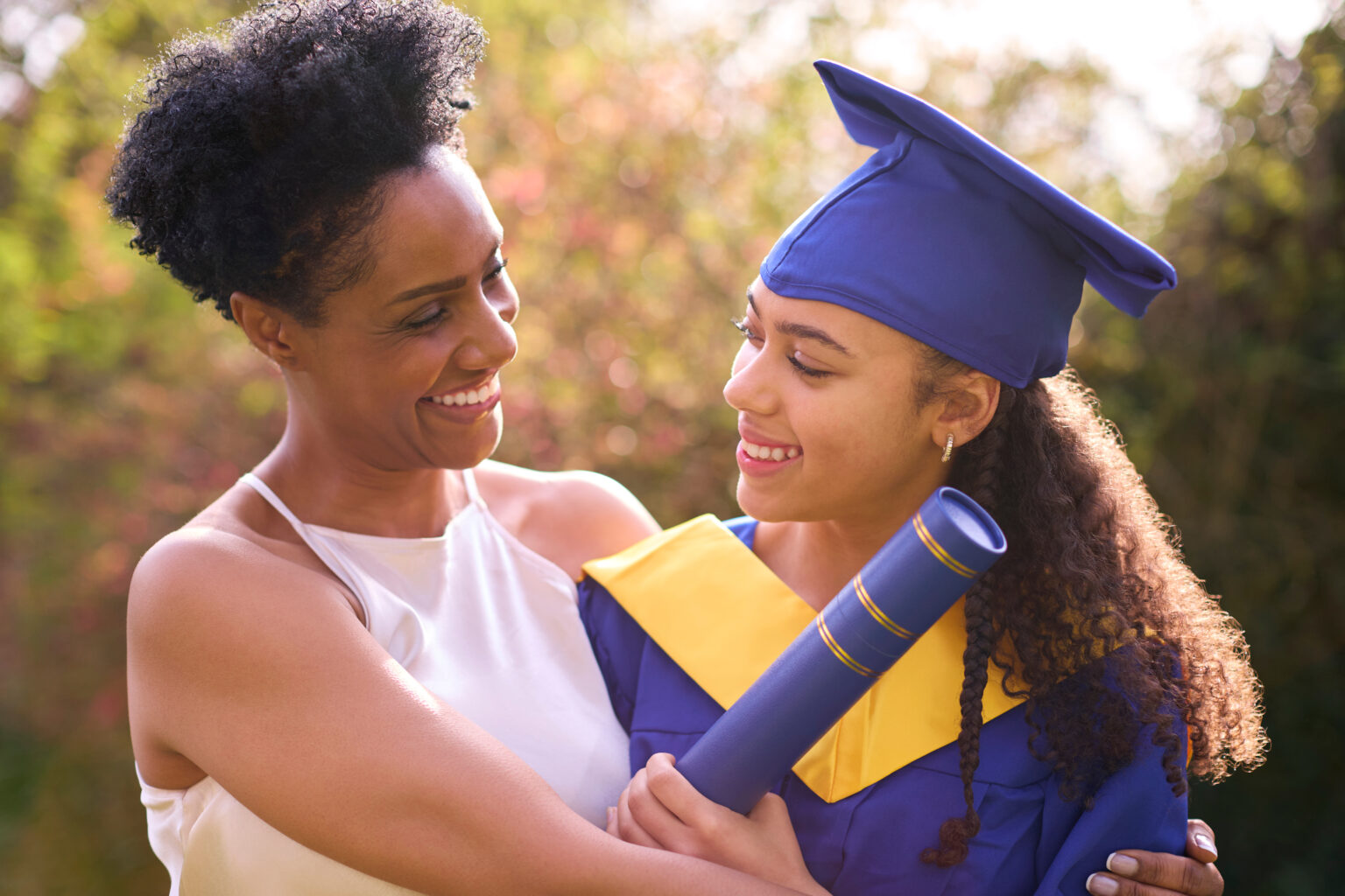proud mother celebrating with teenage daughter wearing graduation robes outdoors